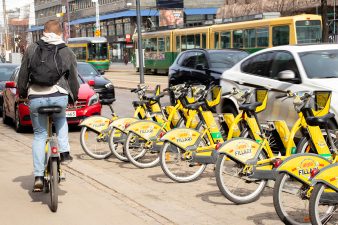 Kaupunkimaisemassa oleva kaupunkipyöräteline ja pyöräilijä, taustalla raitiovaunu.