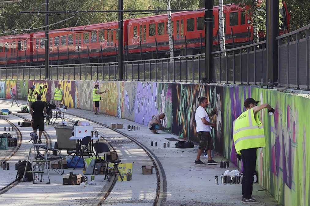 Taiteilijat maalavat graffiteja betonikaukaloon Roihupellossa, taustalla metrojuna.
