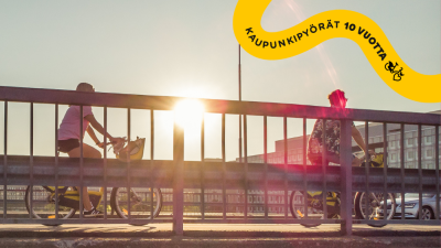 Kaksi pyöräilijää sillalla auringon laskussa.