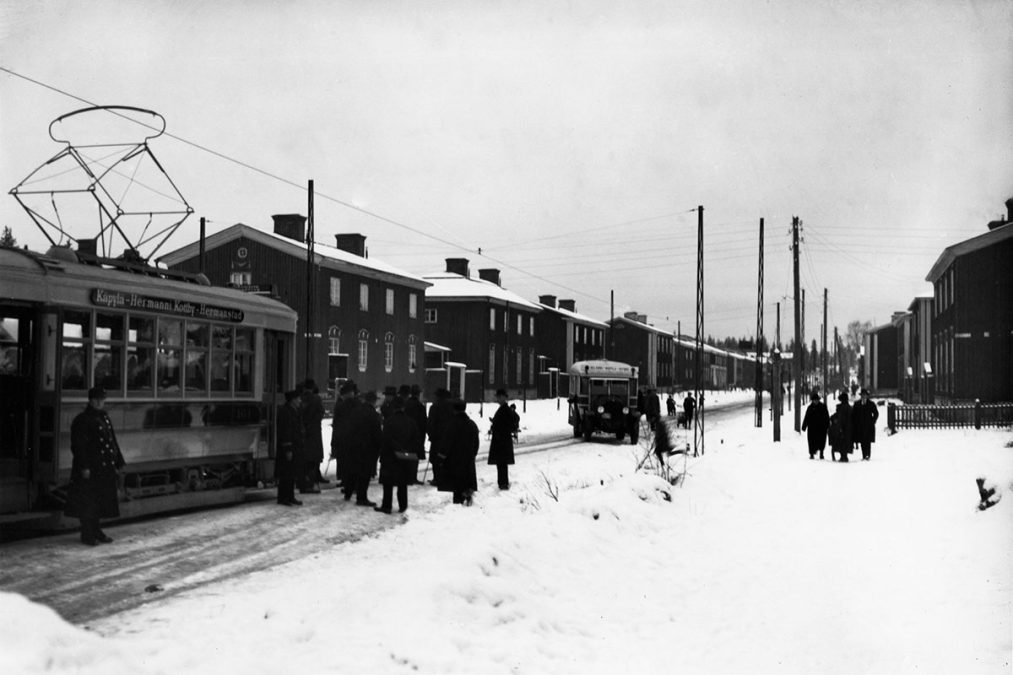 Ensimmäinen raitiovaunu Pohjolankadulla ja Käpylän bussi sekä ihmisiä kadulla.