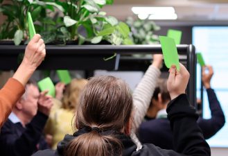 käsiä ylös nostettuina, jotka pitelevät vihreitä post-it -lappuja.