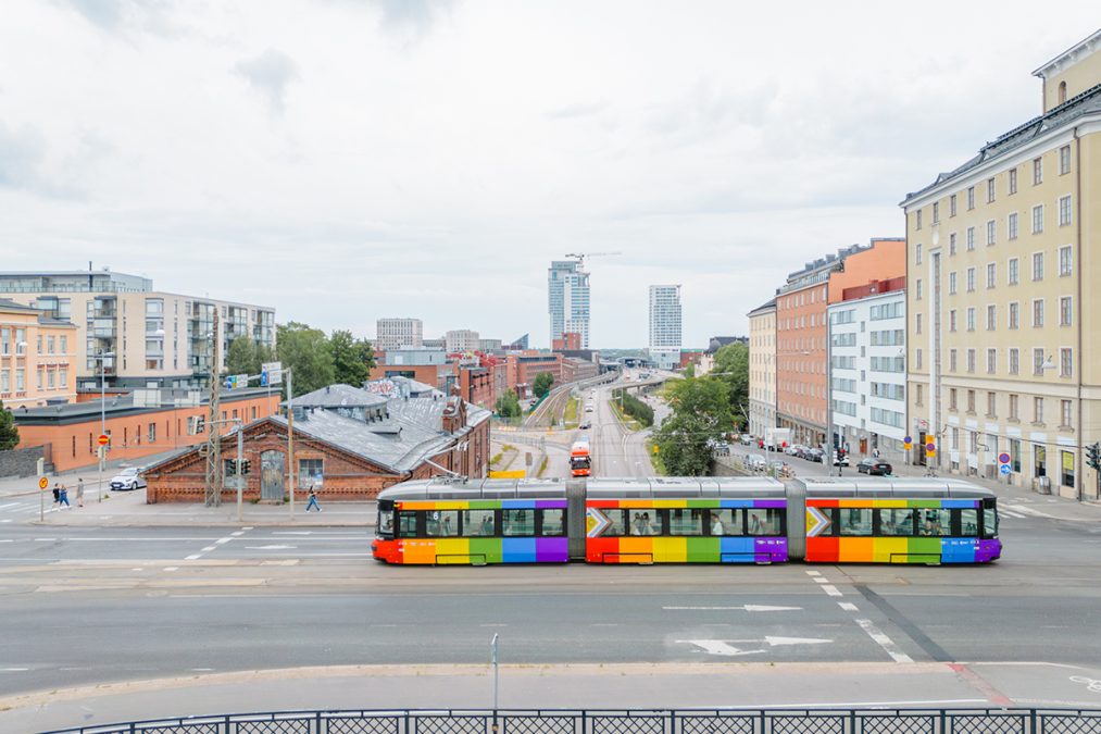 Sateenkaaren värinen raitiovaunu Sörnäisissä Kalasataman tornit taustalla.