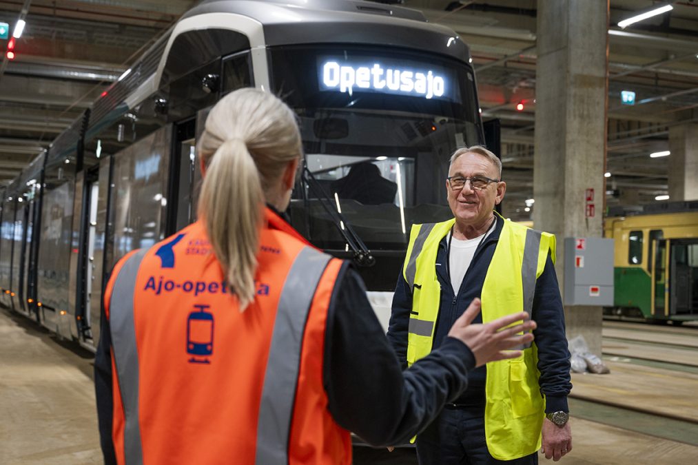 Two people in high-visibility vests in front of a tram.