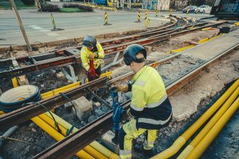 Kaksi miestä korjaa huomiotakeissaan raitiotiekiskoa.