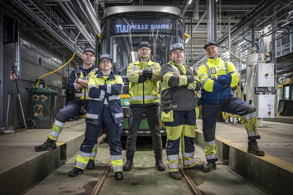 Neljä työntekijää työhaalareissa poseeraa raitiovaunun edessä.