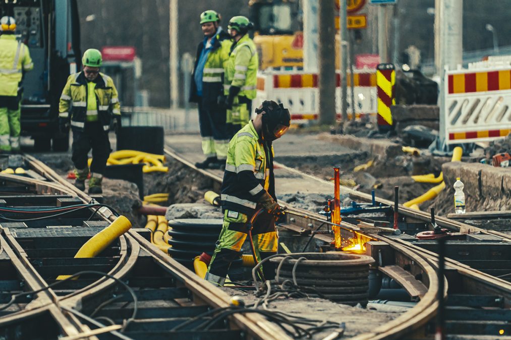 Työntekijöitä huomioasuissa tekee töitä raitiovaunuraiteilla.