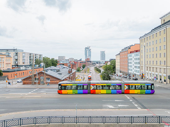 Raitiovaunu, joka on teipattu sateenkaaren väreillä, kulkee kaupungin kaduilla kesäpäivänä.
