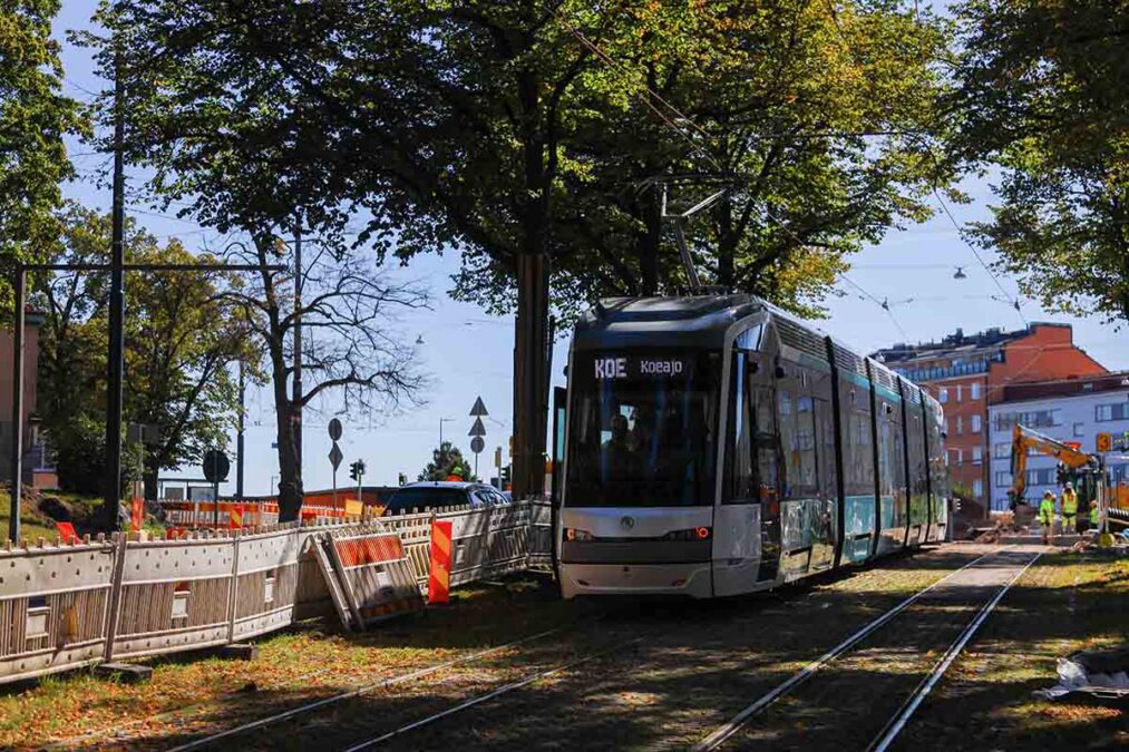 Raitiovaunu koeajoissa Mäkelänkadulla, taustalla työmaa-aitaa ja puita.